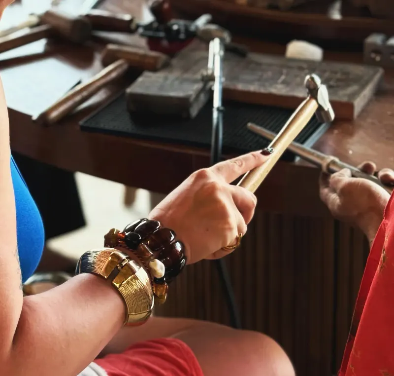 A guest shaping silver with a jeweler's hammer at a Bali Jewelry House workbench